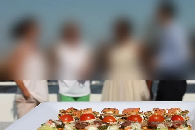 Un vassoio di canapè con salmone affumicato e pomodoro sul ponte di un battello, con ospiti sfocati che bevono sullo sfondo