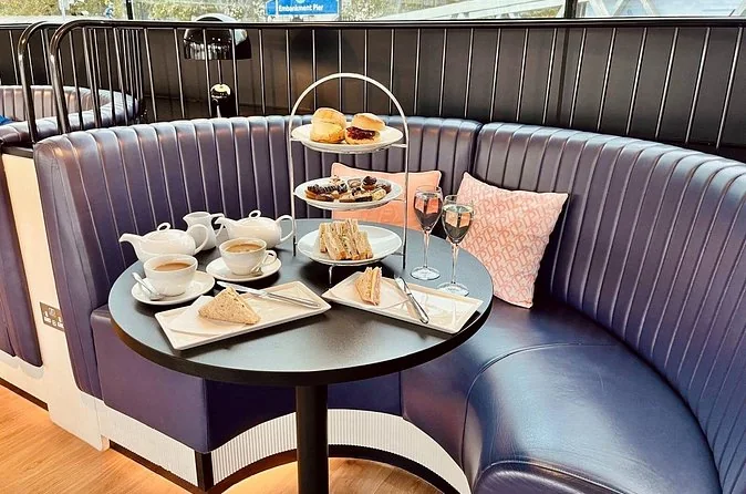 A tiered afternoon tea stand, teapots and two glasses of fizz on a round table in a curved lounge booth
