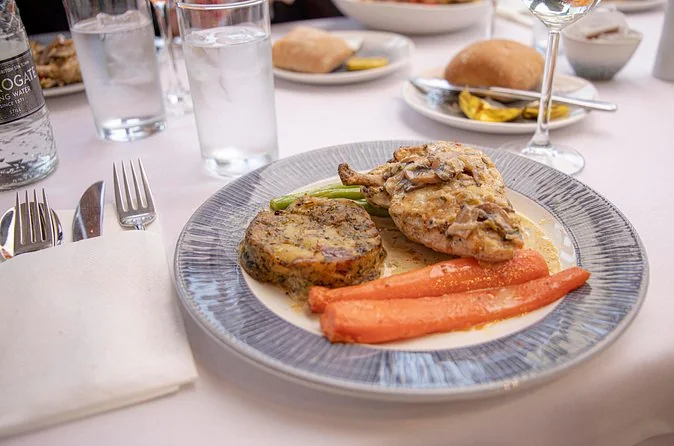 A plated chicken main with mushroom sauce, carrots, green beans and a herb cake on a white tablecloth