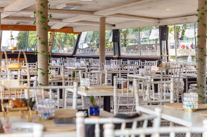 Filas de mesas puestas en el salón comedor de un barco con grandes ventanales a ambos lados